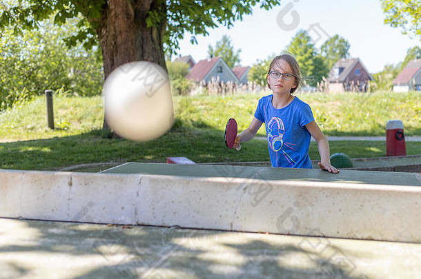 一个9岁的女孩在外面的乒乓球桌上打乒乓球。她正在玩扣球游戏