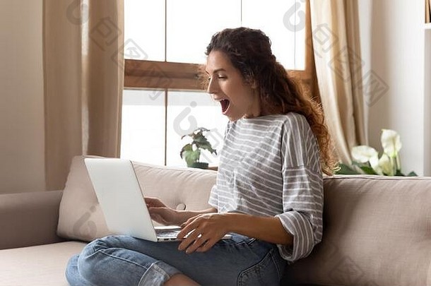 惊讶的年轻女子张着嘴看着电脑显示器。
