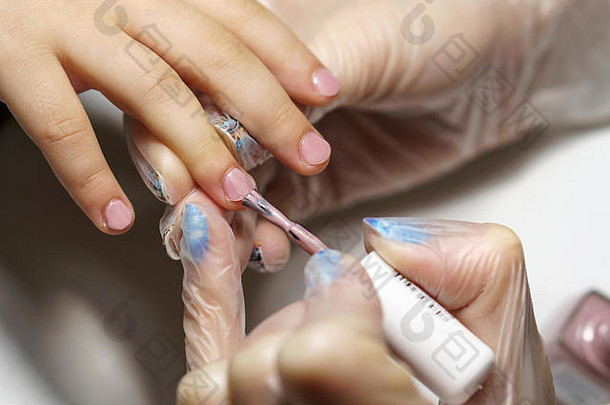 专业儿童美甲。美容师在孩子手指的指甲上涂上愈合和紧致清漆。特写镜头。