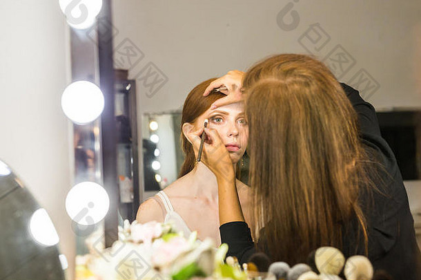 美丽的年轻红发女人用化妆师化妆眼影