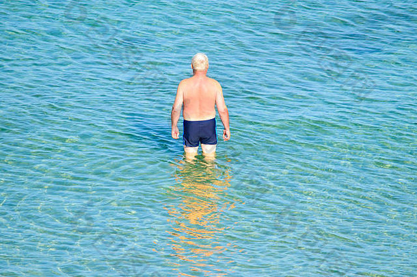 老人站在齐膝深的清澈海水中