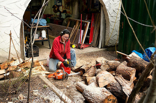 一名妇女在劈柴火取暖时用电锯锯锯。惠斯勒不列颠哥伦比亚省，加拿大。