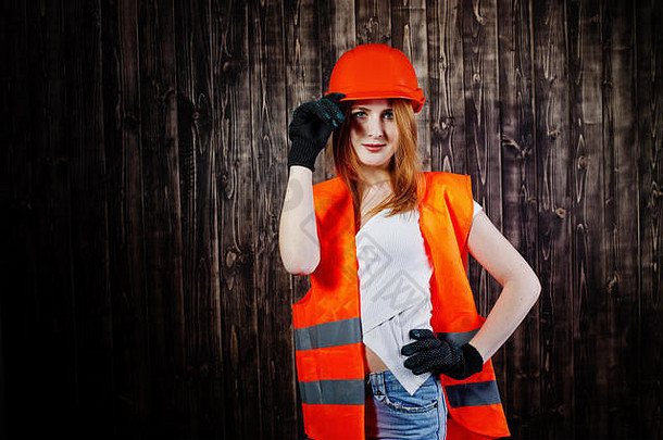 身着橙色头盔和建筑夹克的女工程师在木制背景下保护头盔和建筑夹克。