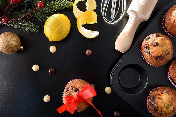 <strong>圣诞</strong>派对用的新鲜巧克力松饼，放在黑桌子上，还有柠檬和厨房用品。水平构图。顶视图。