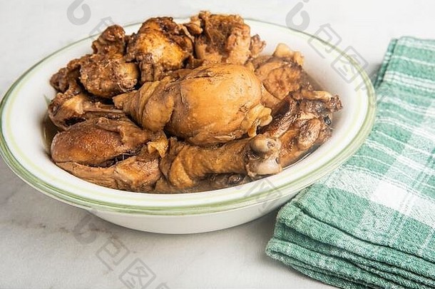 一份菲律宾风格的鸡肉阿多波菜，盛在碗里，绿色餐巾放在大理石桌面上。