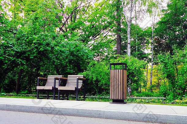 两个独立的木制公园椅子和垃圾桶在绿色公园的人行道边上
