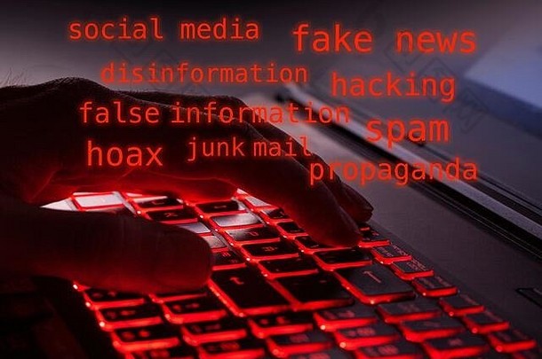 在黑暗中，手指在电脑键盘上的红色背光键上打字的特写镜头。关于电脑黑客、假新闻、反欺诈的红字