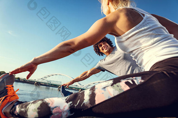 特写镜头年轻的快乐跑步者夫妇培训在户外河伸展运动腿日落