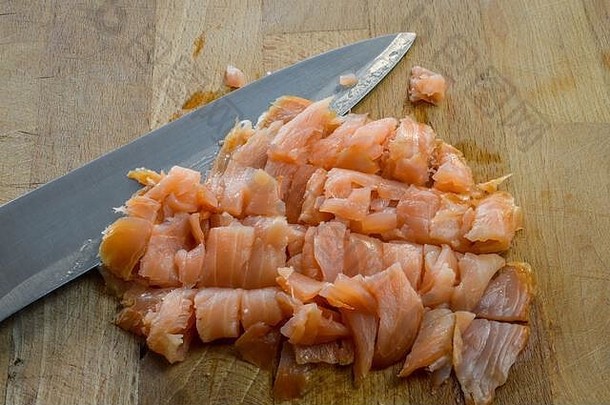 用菜刀在木制砧板上切碎新鲜熏鲑鱼。