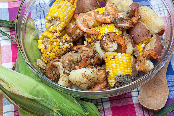 一个玻璃碗里装满了玉米棒、红土豆和虾——一种典型的虾煮法。