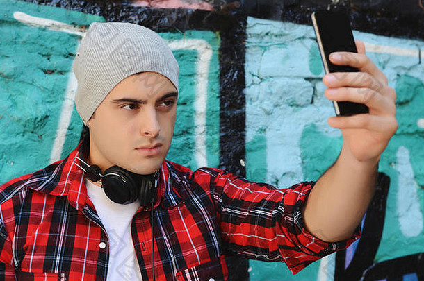 年轻的拉丁男子在街上用智能手机自拍。