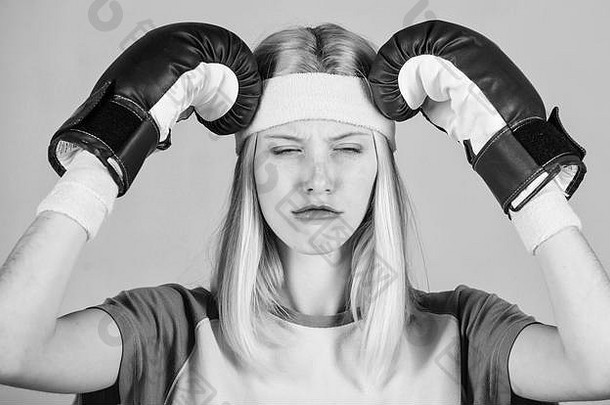 头痛的概念。保持镇静，消除头痛。治头痛。女孩打拳击手套累了。坚强的女人承受痛苦。头痛疗法。女孩痛苦的脸用拳击手套抱着头。