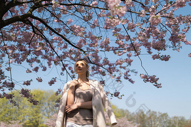 春天，樱花公园里美丽的金发女郎穿着休闲服，在旅游途中享受自然和自由时光