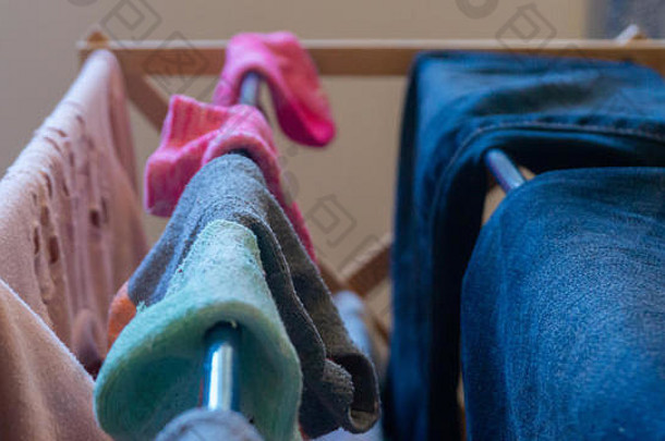 在起居室的室内，一双不相配的踝袜在洗衣架上晾干，里面有女人的衣服，包括蓝色牛仔裤和粉色孔<strong>眼毛</strong>衣。