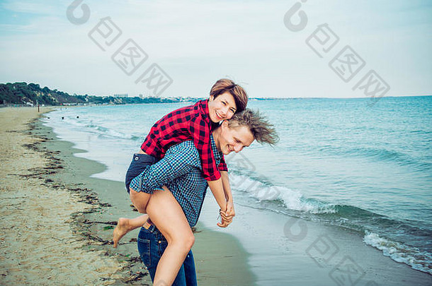 年轻男子在海滩上背着女人骑马。这对年轻夫妇在蓝色海洋背景下<strong>一起</strong>玩得很开心。情人节快乐时光的概念