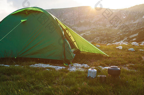 日出时，在草地上用茶壶和帽子露营。保加利亚的山脉。