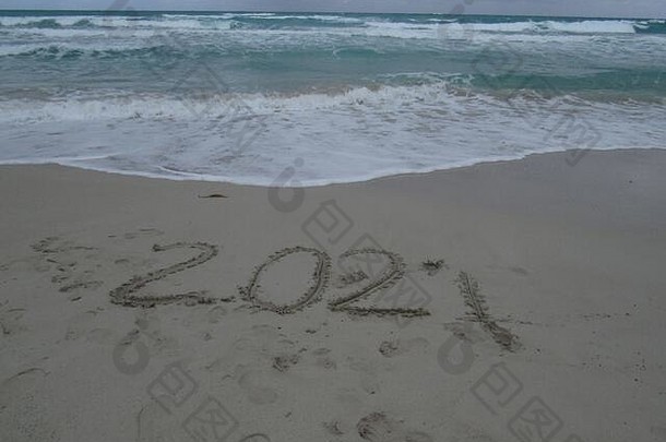 新年快乐2021，在海滩上挥舞着波澜碧蓝的大海。数字2021年在海边，信息写在金色沙滩上