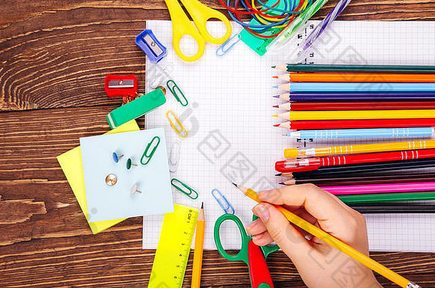 打开空白笔记本，手拿毛笔，在木制书桌的背景上放着一个学校用品的框架。将拷贝空间返回到sch