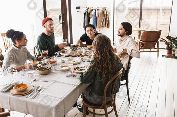 年轻的<strong>国际友人</strong>坐在满桌食物的桌旁，梦幻般地相互交谈。一群同事一起吃午饭