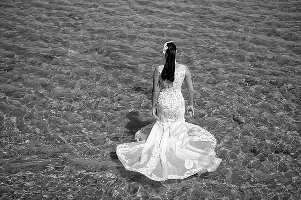 海上蜜<strong>月度</strong>假村。国外婚礼。婚礼在海边举行。新娘白色婚纱站在海水中。湿漉漉的婚纱在炎热的阳光下。新娘快乐享受暑假海洋背景。