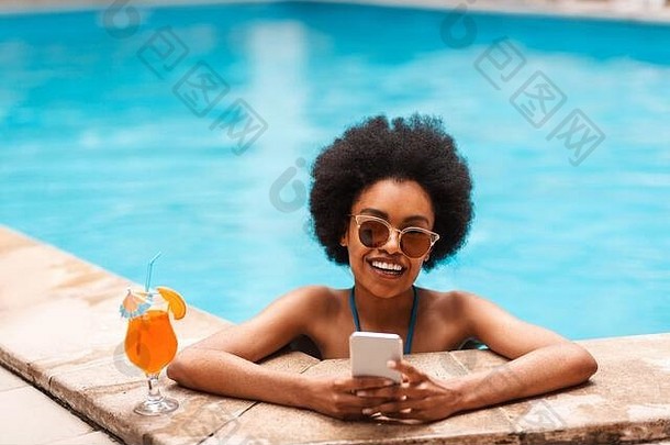 快乐的黑人女孩，在阳光明媚的日子，喝着清新的夏日鸡尾酒，在游泳池里放松，在空白处