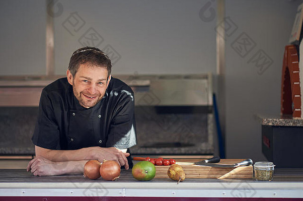 厨房里微笑的男<strong>厨师</strong>倚在柜台上，拿着烹饪原料