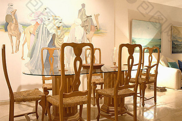 在七十年代的餐厅里，拉什坐着的椅子和玻璃顶的桌子，柱子上画着大图