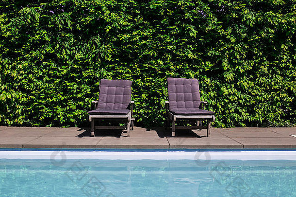 在炎热的夏日，现代别墅的蓝色豪华游泳池配有沙发