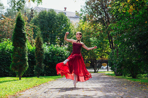 在秋季公园，一位身着红色芭蕾舞服、穿着尖头鞋跳舞的女芭蕾舞演员。