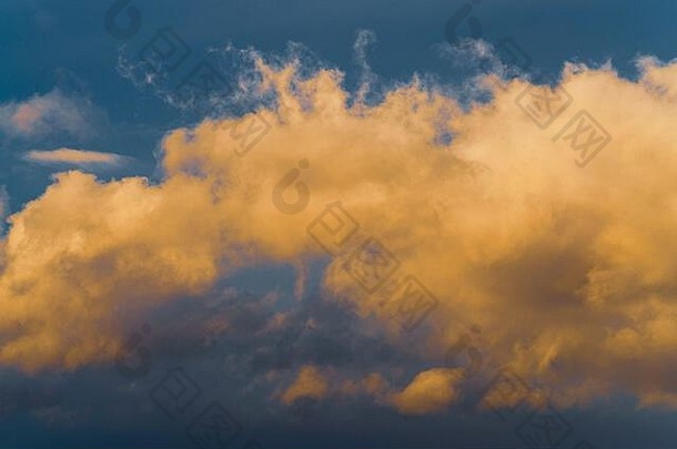 美丽的金色蓬松的云在日落时被消失的光线照亮，雷雨云在晴朗的蓝天上飘浮，以改变季节天气。纳图
