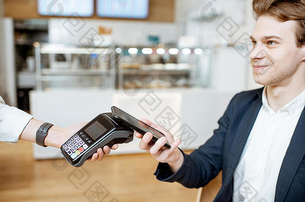 坐在咖啡馆里用智能手机支付非接触式费用的年轻商人