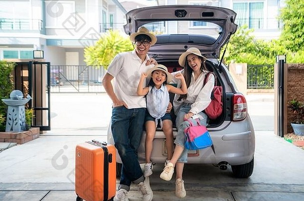 这张照片是一个亚洲家庭，父亲、母亲和女儿在为度假准备手提箱时，看上去很开心。在车库里拍的。