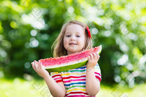 孩子在花园里吃西瓜。孩子们在户外吃水果。儿童健康零食。小女孩在花园里玩耍，咬着一片水