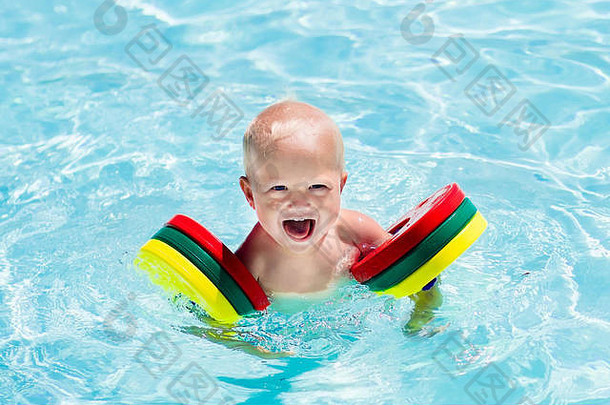 在一个炎热的夏日，快乐欢笑的小男孩在室外游泳池里玩耍。孩子们学习游泳。戴着五颜六色臂章的孩子。