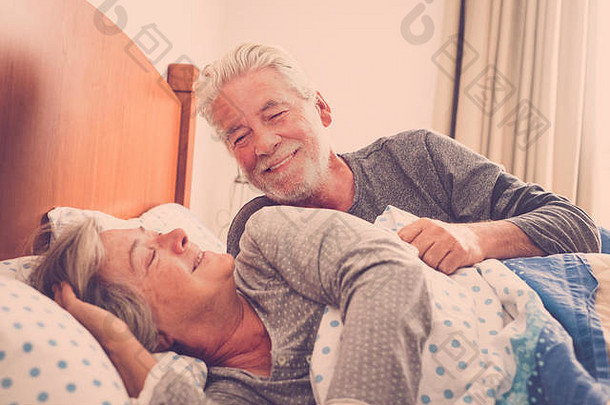 一对老年夫妇在床上休息，微笑着享受着醒来的时光。快乐的退休白人男女