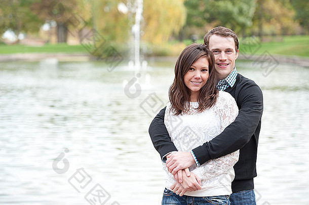 阳光明媚的日子里，一对迷人的年轻夫妇在池塘边摆姿势。