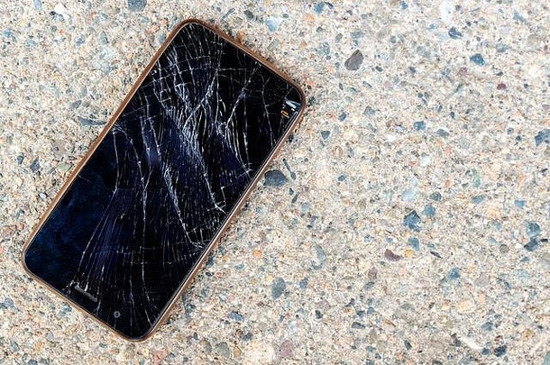 一部破碎的手机躺在水泥人行道上。手机屏幕被打碎了。电话无法识别。