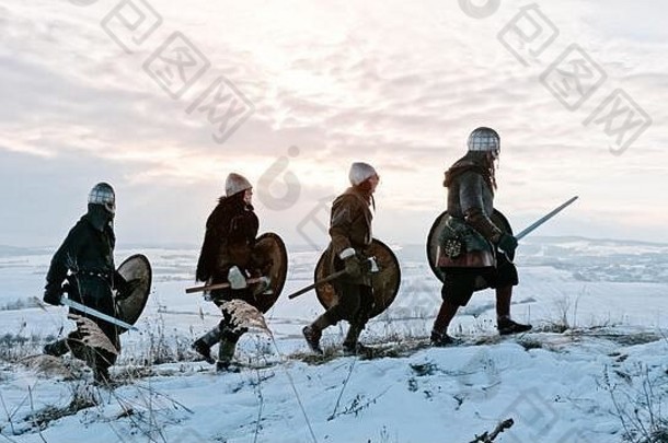 一群拿着盾牌和剑的维京人在冬天的草地上前进。男，领导。
