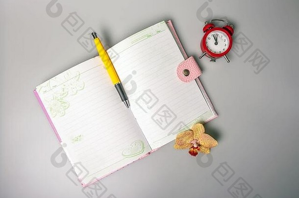 桌上放着一本打开的笔记本、一支笔、一朵兰花和一个让人想起时间的闹钟。办公室学校用品。放置文本。俯瞰