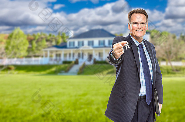 房地产经纪人拿着房子钥匙在美丽的房子前面。