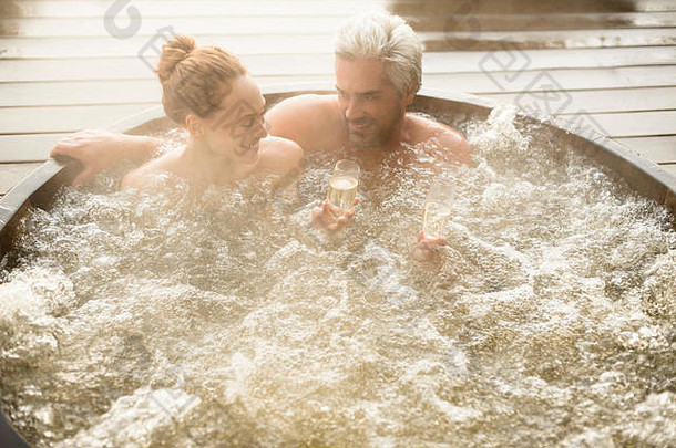 微笑的夫妇在露台上的热浴缸里喝香槟