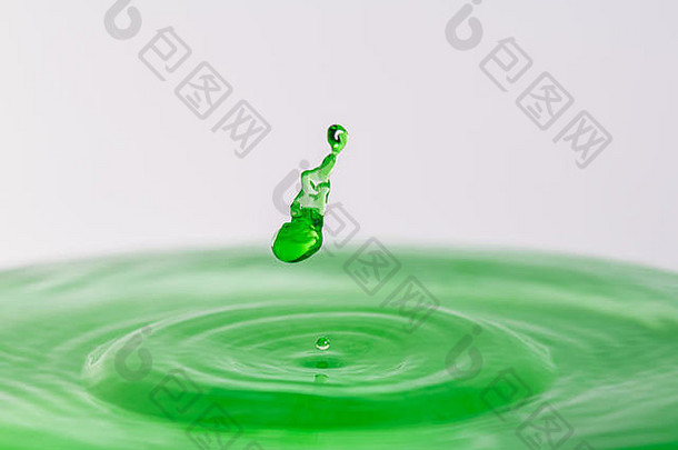 一个绿色水滴在浅色白灰色背景下溅入水中的特写微距摄影