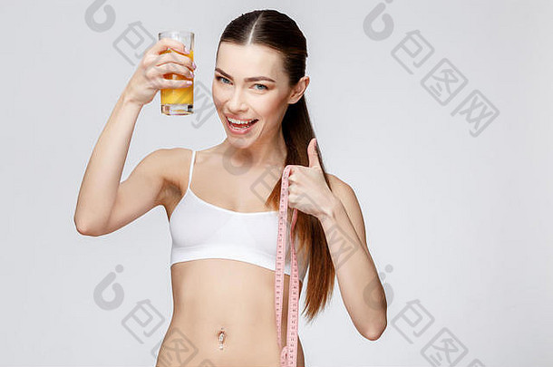 灰色背景下的运动型女人，手里拿着一杯橙汁