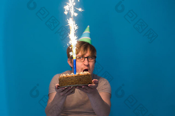 戴着眼镜、戴着纸帽子、手里拿着燃放烟火的蛋糕的疯狂快乐的学生。节日生日概念