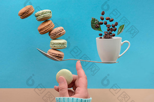 完美平衡概念构图。用手指平衡一杯咖啡和macaronos，平放在蓝色薄荷色的纸上