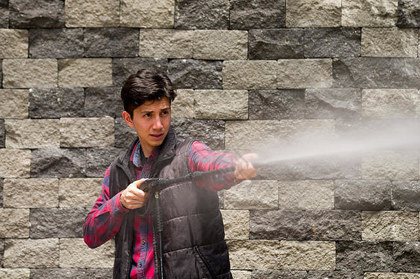 一个英俊的年轻人穿着方形的红色衣服，手持高压水，背景是灰色的砖墙