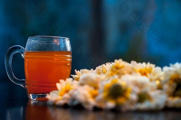 一个玻璃杯子里的菊花茶的特写镜头，在黑色木板上有一些普通的菊花。背景模糊的水平镜头