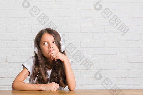 年轻的西班牙裔小孩戴着耳机坐在桌子上认真地思考着问题，很困惑的想法