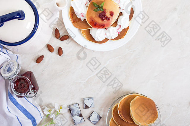 美味的煎饼，配覆盆子酱和鲜奶油，放在餐桌上的白色盘子上。经典的美国早餐。顶视图