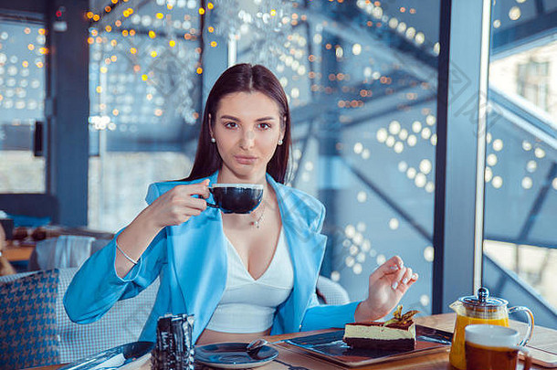 在曼哈顿，年轻漂亮的女人在家里吃甜点喝咖啡的画面。穿着正式蓝色套装的西班牙裔女孩坐在桌子旁